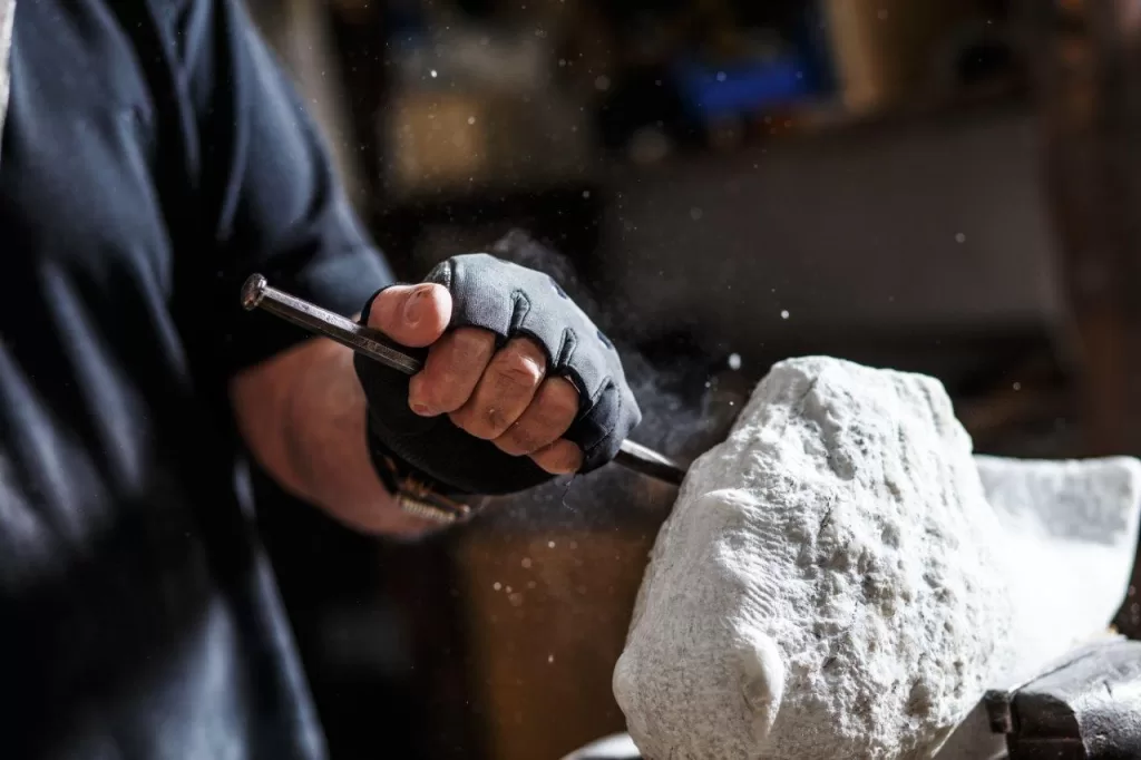 Senior sculptor working on his granite sculpture in his workshop with hammer and chisel
