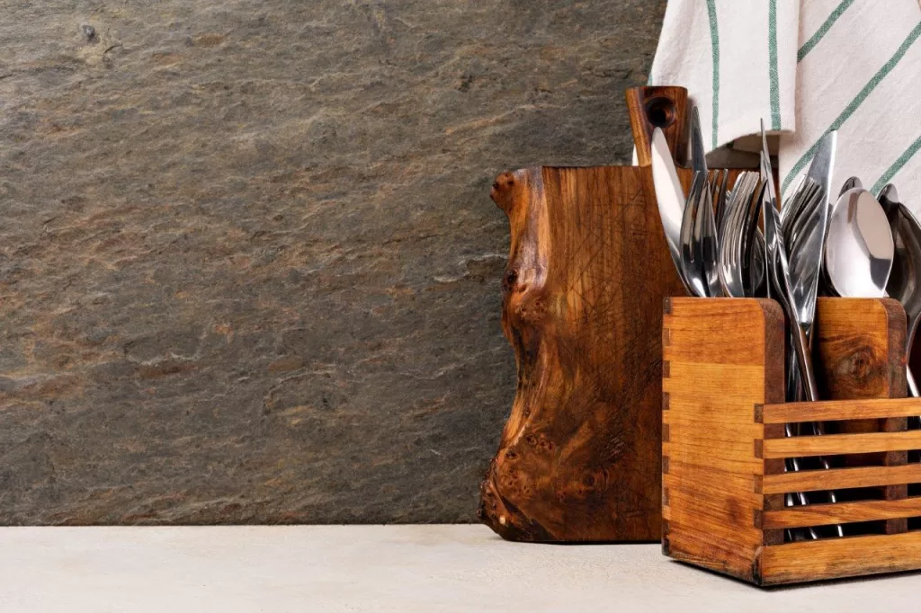 Cutting board and cutlery on wooden kitchen table next to rough slab of granite